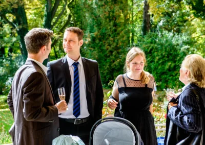 Gespraech bei einer Hochzeit im Freien, vier Gaeste stehen zusammen, halten Getraenke. Hochzeitsfotografie Feldafing.