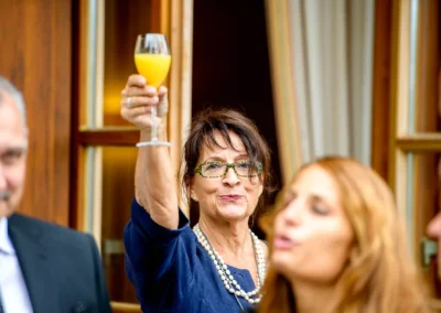 Frau erhebt ein Glas Saft bei Hochzeitsfeier nahe Tegernsee. Hochzeitsfotografie, lebendiger Moment eingefangen.