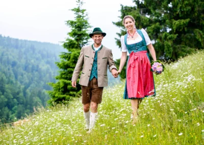 Brautpaar in traditioneller Tracht auf Blumenwiese bei Bayrischzell, Hochzeitsfotografie in malerischer Umgebung.