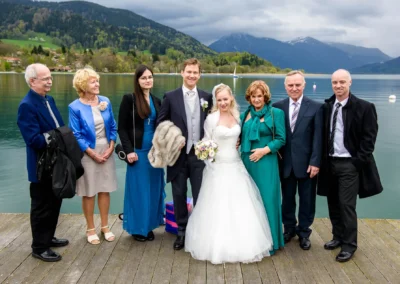 Brautpaar mit Familie am Tegernsee zur Hochzeitsreportage. Elegante Kleidung und See im Hintergrund.