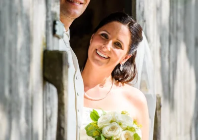 Brautpaar laechelt in die Kamera, Braut mit Blumenstrauss. Hochzeitsfotografie in Oberbayern.