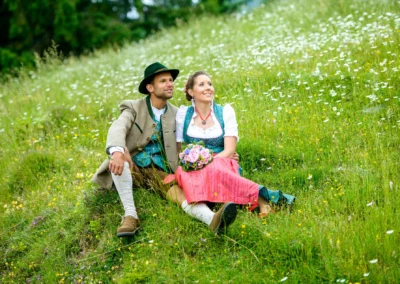 Brautpaar in traditioneller Tracht sitzt auf Wiese, Hochzeitsfoto im Sillberghaus, Bayrischzell.