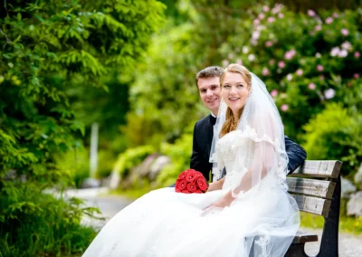 Brautpaar auf Bank im Gruenen mit roten Rosen, Hochzeitsfotografie nahe Zugspitze.