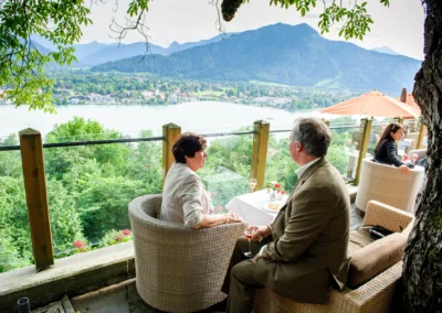 Paar bei einer Hochzeit am Tisch mit Blick auf den Tegernsee im Leeberghof. Hochzeitsfotografie in natuerlicher Umgebung.