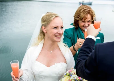 Braut und Gaeste beim Anstoßen mit Sekt. Hochzeitsfoto in Gmund am Tegernsee mit strahlendem Laecheln der Braut.