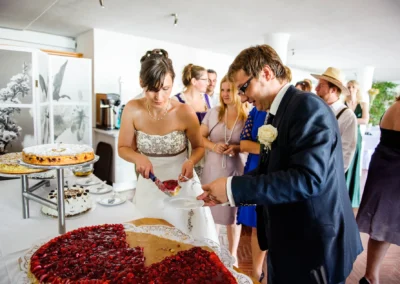 Brautpaar schneidet Kuchen bei Hochzeitsfeier nahe Chiemsee. Hochzeitsfotografie zeigt Detail der Feierlichkeiten.