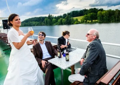 Braut und Gaeste bei der Hochzeitsfeier auf einer Schifffahrt am Staffelsee mit Blick auf den See. Hochzeitsreportage.