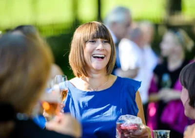 Lachende Frau bei Hochzeitsfeier im Schlossgut Oberambach, umgeben von Gaesten mit Getraenken.