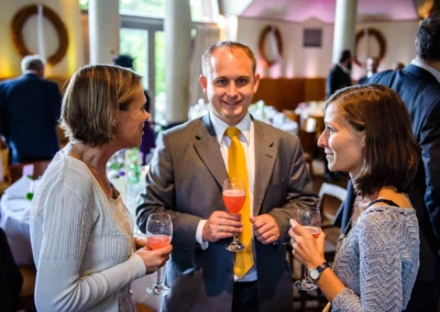 Gespraech von drei Gaesten mit Getraenken bei einer Hochzeit im Seehaus, festgehalten von einem Hochzeitsfotografen.