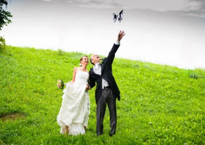 Brautpaar wirft Schmetterling in die Luft bei Hochzeit auf gruenem Hang in Oberbayern. Hochzeitsfoto voller Freude.