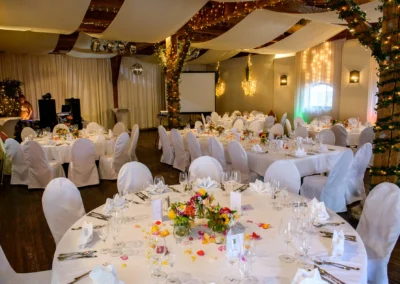 Elegante Hochzeitsdekoration in Moosach mit runden Tischen, weissen Stuhlhussen und Blumenarrangements.