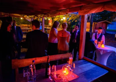 Gesellschaft bei einer Hochzeit im Paulaner Seegarten mit Kerzenlicht und Getränken auf einem Holztisch. Hochzeitsreportage.