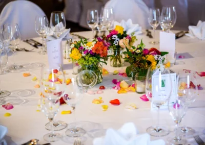 Hochzeitsfotografie in Muenchen: Eleganter Tisch mit bunten Blumenarrangements und Gläsern bei einer Hochzeitsfeier.