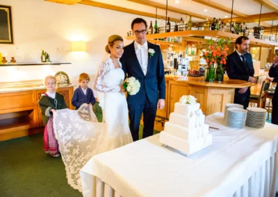 Brautpaar neben Hochzeitstorte, assistiert von Kindern, bei Hochzeitsreportage in Waakirchen.