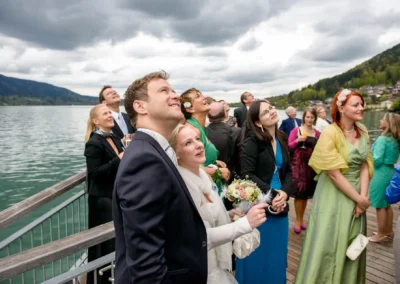 Hochzeitsfotografie am Tegernsee: Gäste blicken staunend auf, während die Braut einen Blumenstrauß hält.