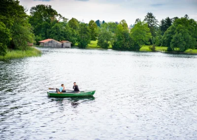 Paar in Ruderboot auf Staffelsee bei Hochzeit, umgeben von malerischer Natur und Bootshausern. Hochzeitsfotografie.