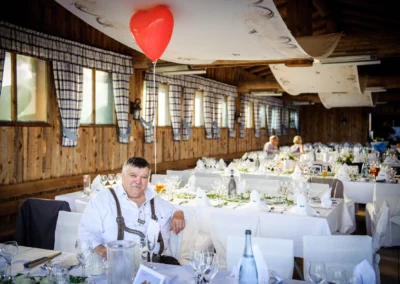 Älterer Mann in Tracht bei Hochzeitsfeier auf Sprengenoeder Almvin Eurasburg; gedeckte Tische mit Herzballon und Dekoration.