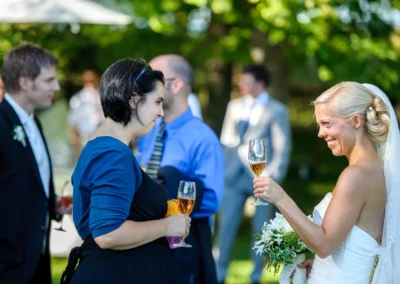 Braut mit Blumenstrauss spricht bei Hochzeitsfeier in Oberambach mit Gast, Hochzeitsfotografie im Freien.