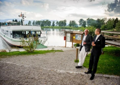 Hochzeitsfoto mit zwei Gaesten vor einem Schiff am Staffelsee. Hochzeitsreportage dokumentiert die besondere Feier.