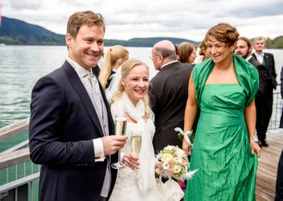 Brautpaar mit Gaesten feiert Hochzeit am Tegernsee. Hochzeitsfotografie zeigt froehliche Momente und festliche Kleidung.