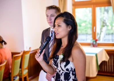 Junge Frau haelt Mikrofon bei Hochzeitsfeier im Leitzachtal, Mann unscharf im Hintergrund sichtbar. Hochzeitsfotografie.