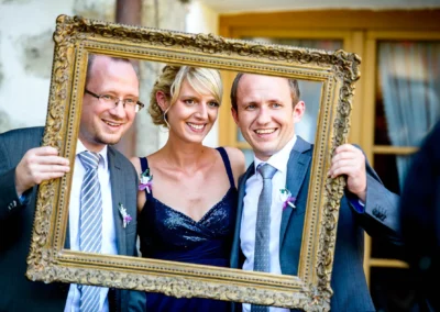 Drei Personen halten einen antiken Bilderrahmen bei einer Hochzeit nahe Rosenheim. Hochzeitsfotografie im Freien.