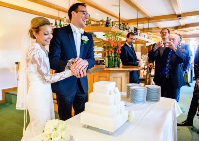 Brautpaar schneidet Hochzeitstorte in Waakirchen vor Gaesten bei einer Hochzeitsfeier, eingefangen von Hochzeitsfotografie.