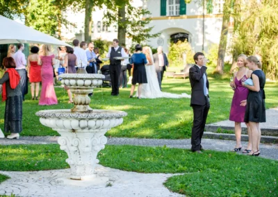 Gartenempfang bei Hochzeit mit Springbrunnen im Vordergrund, Gaeste plaudern, Schlossgut Oberambach nahe Starnberger See.