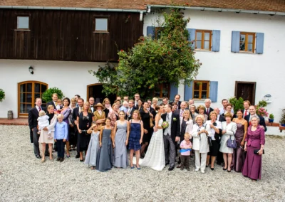 Hochzeitsfoto auf Gut Thurnsberg: Brautpaar mit Hochzeitsgesellschaft vor einem Haus in Oberbayern.
