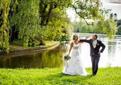 Brautpaar tanzt am Kleinhesseloher See in Schwabing bei einer Hochzeitsfotoreportage, umgeben von gruenem Wald.