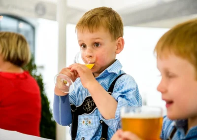 Junge in Tracht bei Hochzeit in Muenchen trinkt Orangensaft, Hochzeitsreportage Fasanerie Moosach.