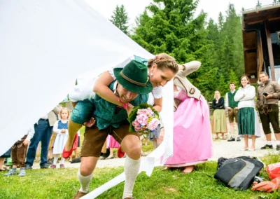 Brautpaar in traditioneller Tracht passiert ein zerschnittenes Laken, Hochzeitsreportage in Bayrischzell.