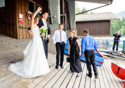 Brautpaar mit Freunden auf Holzsteg am Eibsee, Jubel und Freude bei der Hochzeitsfotografie.