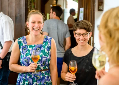 Gäste lachen bei einer Hochzeit in Moosach, mit einem Glas Wein. Hochzeitsfoto von Hochzeitsfotograf in München.