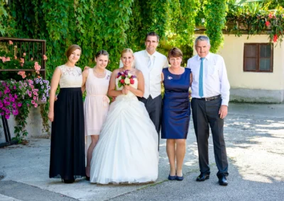Brautpaar mit Familie vor gruener Wand bei Hochzeit nahe Rosenheim. Hochzeitsfotograf erstellt Hochzeitsreportage.