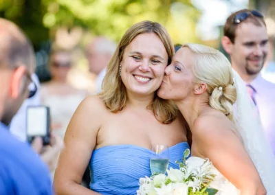 Braut küsst Gast bei Hochzeitsfeier in Oberambach, Brautstrauss und Sektglas in der Hand, Hochzeitsfotografie.
