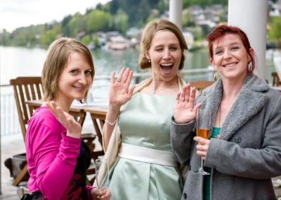 Drei lachende Frauen bei einer Hochzeitsreportage am Tegernsee, heben die Haende zur Kamera. Hochzeitsfotografie.
