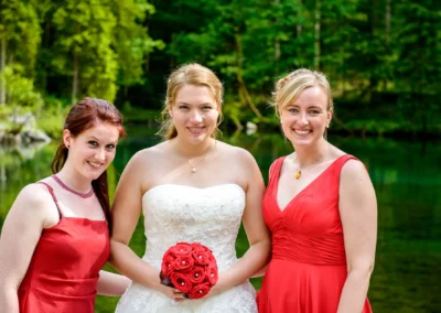 Braut mit Brautjungfern in roten Kleidern am See nahe Zugspitze, Hochzeitsfotografie im Kreis Garmisch-Partenkirchen.