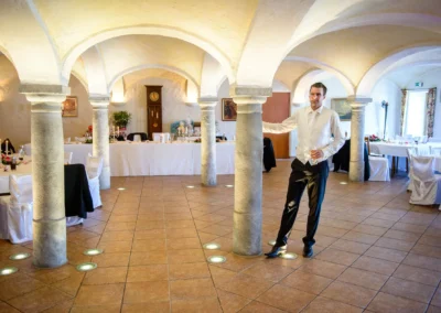 Eleganter Saal mit gedeckten Tischen, Bräutigam lehnt an Säule. Hochzeitsfotograf in Oberbayern auf Hochzeit.
