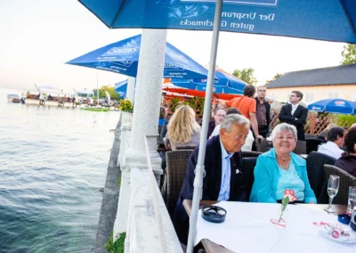Hochzeitsfoto bei Hugos Beach Club, Gaeste am Tisch mit Blick auf Starnberger See unter Sonnenschirmen.