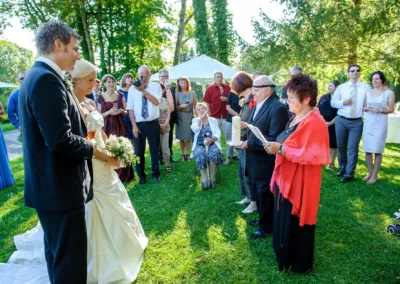 Brautpaar und Gaeste bei Outdoor-Hochzeitszeremonie in Oberambach, Hochzeitsfotografie unter blauem Himmel.