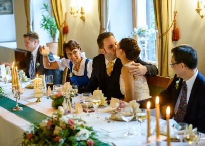 Hochzeitsfoto: Brautpaar bei Tisch, umgeben von Gaesten, nahe Schliersee, aufgenommen von Hochzeitsfotograf.