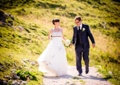 Brautpaar spaziert Hand in Hand auf sonnigem Weg im Chiemgau bei Hochzeitsfotografie.