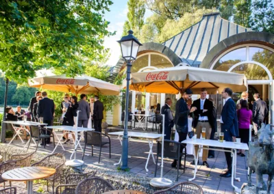 Gäste im Gespräch bei einer Hochzeitsfeier im Freien nahe Kleinhesseloher See, festgehalten von einem Hochzeitsfotografen.