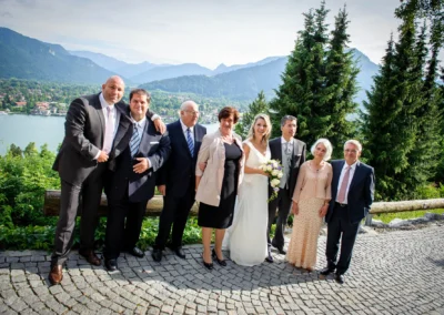 Hochzeitsfoto am Tegernsee: Brautpaar mit Familie und Freunden vor malerischer Bergkulisse im Leeberghof.