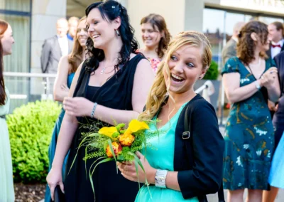 Gäste lachend bei einer Hochzeit in Starnberg, eine Frau mit Blumenstrauss. Hochzeitsfotografie voller Freude.