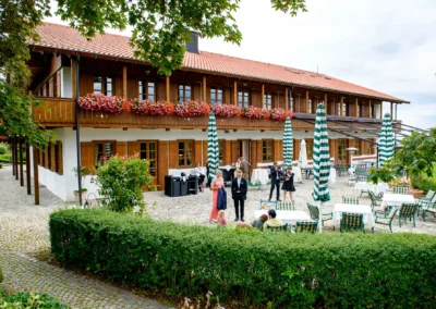 Hochzeitsfoto in Waakirchen: Gäste auf festlich geschmückter Terrasse eines traditionellen Gebäudes bei Hochzeit.