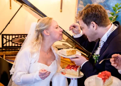 Brautpaar genießt Hochzeitstorte vor einem Flügel bei einer Hochzeitsreportage am Tegernsee.
