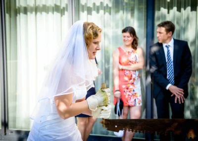 Braut saeumt Holz bei Hochzeitsfoto, Gaeste schauen zu, Aufnahmen bei Hochzeit in Starnberg.