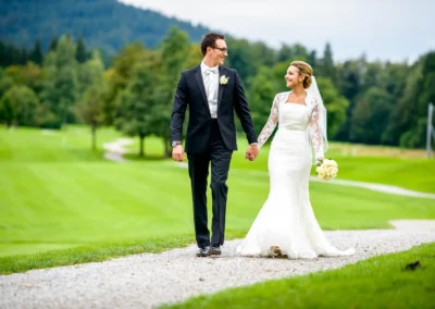 Brautpaar bei Hochzeits-Portrait in Margarethenhof, nahe Tegernsee, Haende haltend auf gruenem Feldweg.